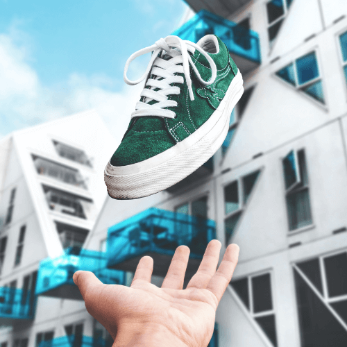 Green suede shoes being thrown into the air with apartments in the background