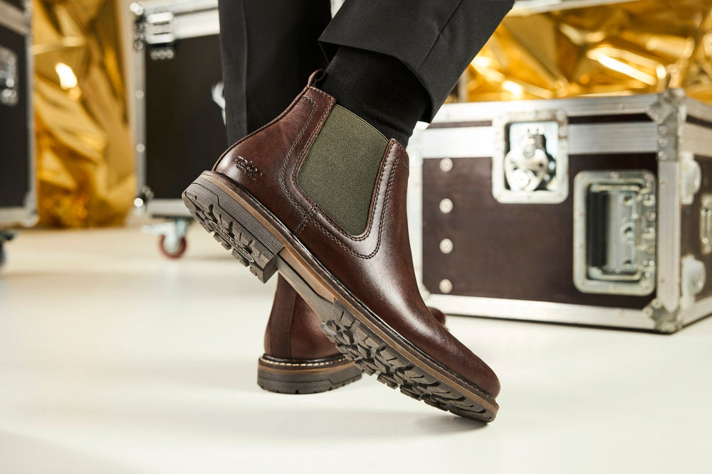 close up of a pair of dark brown mens chelsea boots by Rieker with metal chest in the background surrounded by gold