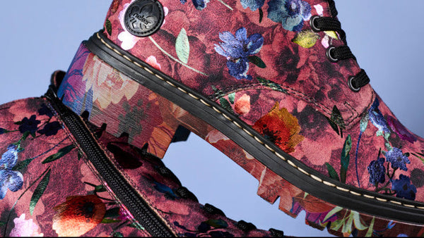 A close-up of a floral lace-up boot with a pink and red watercolor floral pattern, black sole, and black laces, shown against a solid light blue background.